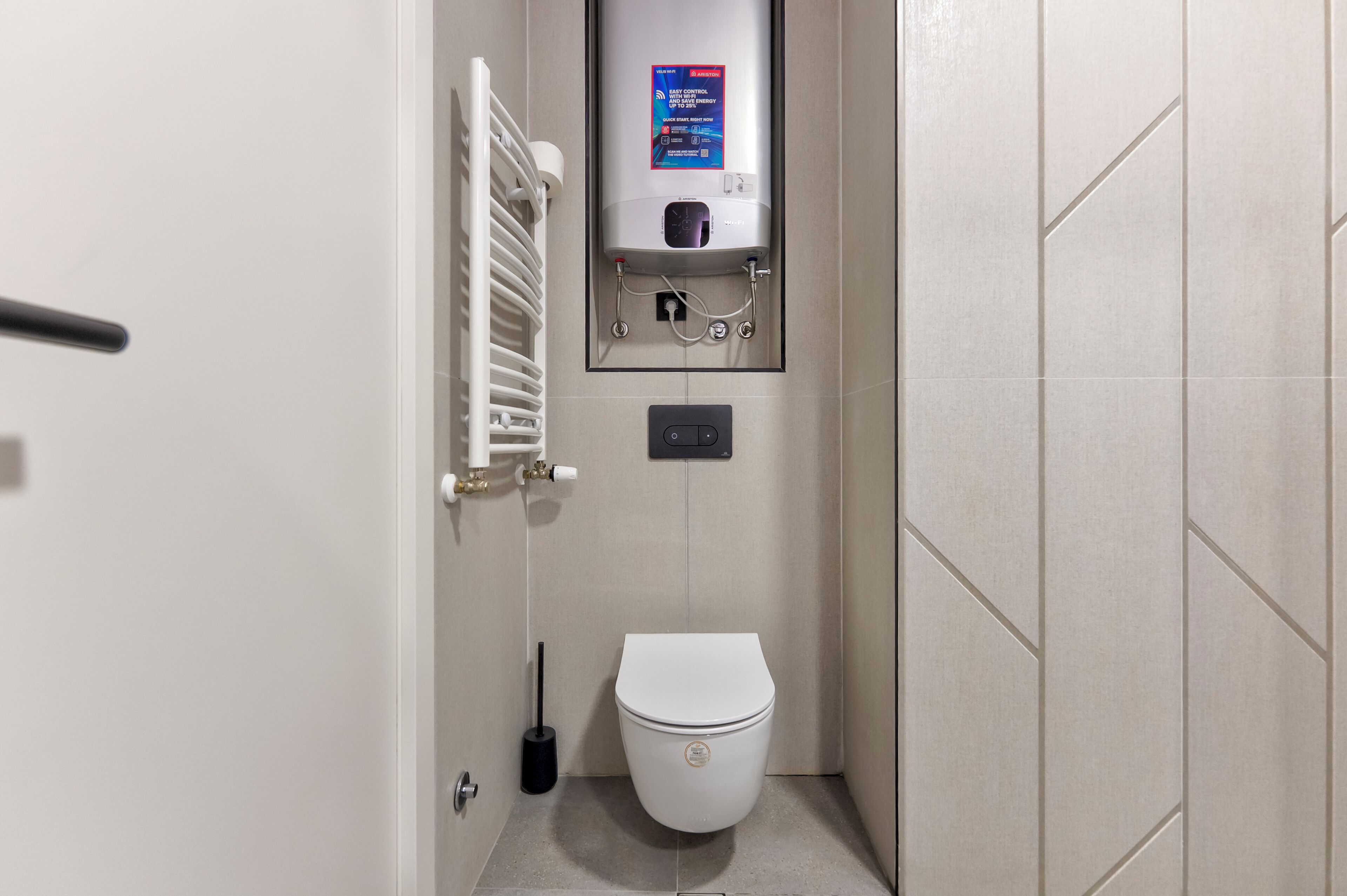 A small bathroom with a toilet, a wall-mounted heater, and a control panel.