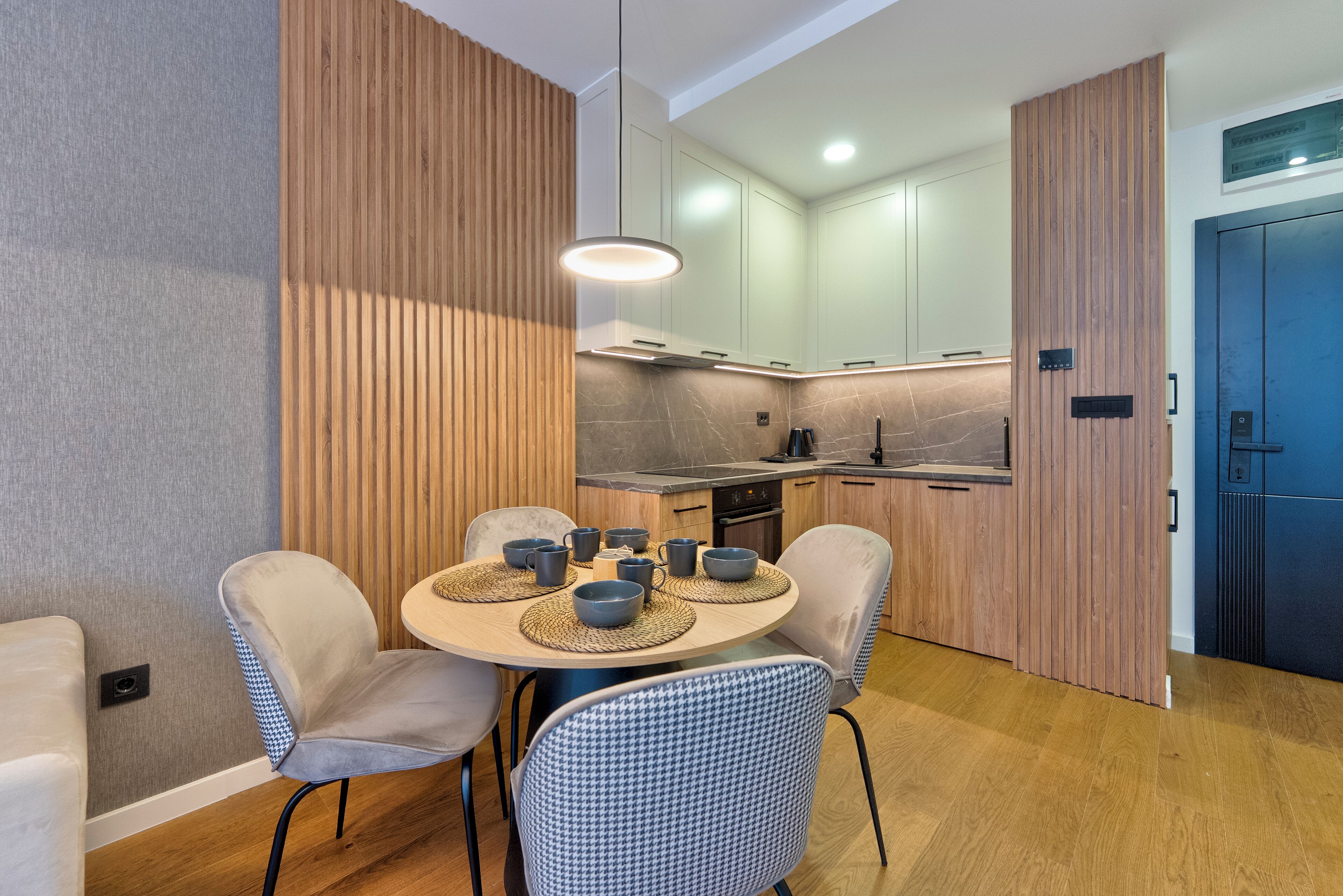 A modern kitchen with a round dining table, chairs, and a hanging light fixture.