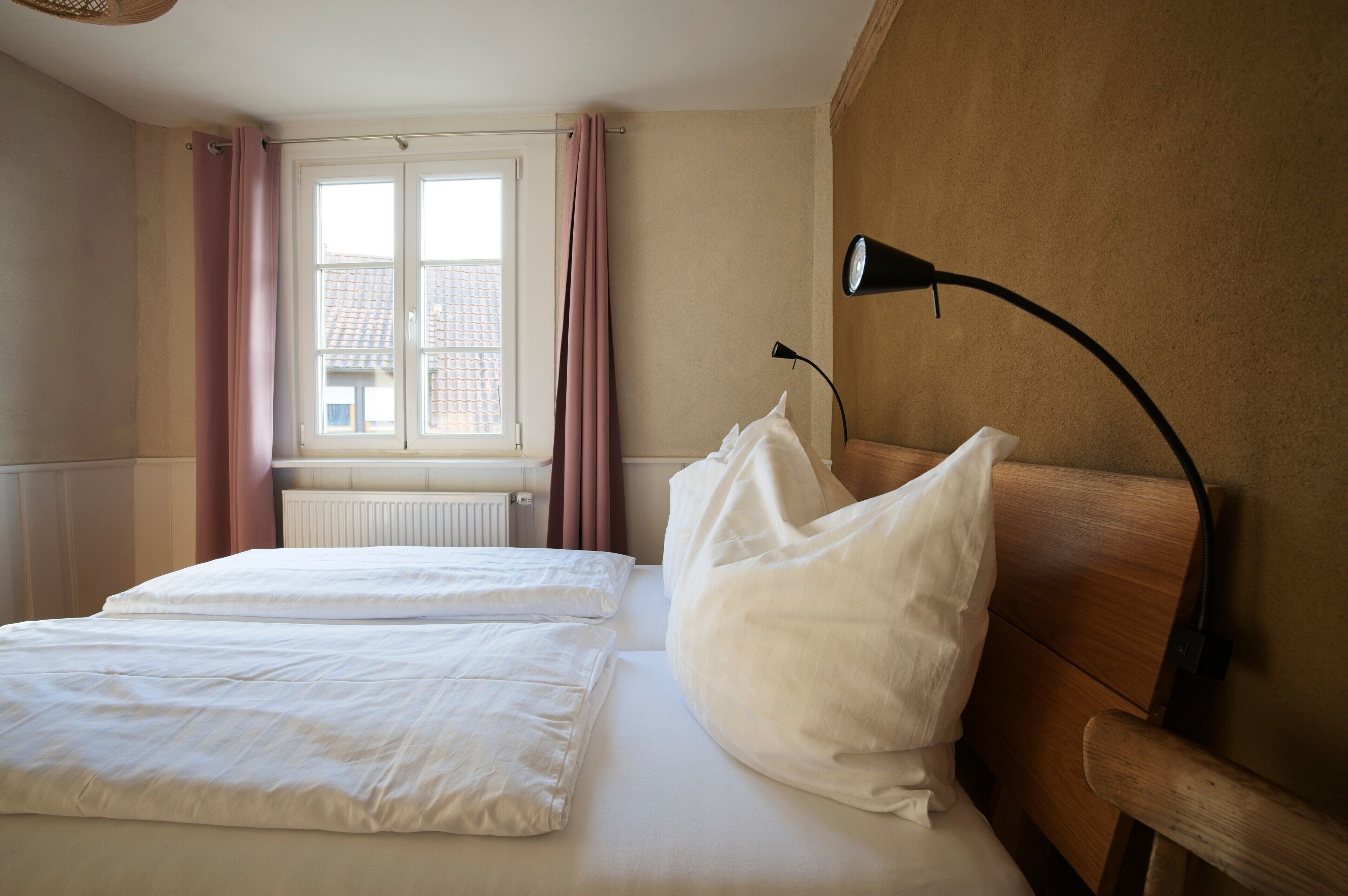 A hotel room with a bed, a bedside lamp, a window with curtains, and a radiator.