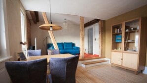 A dining area with a wooden table and chairs, a blue sofa, and a wooden cabinet with shelves. - Apartment 'Klein' with Shared Garden and Wi-Fi (Offenburg)