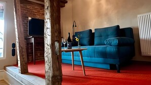A living room with a blue sofa, a wooden table with a bottle and glass, a TV, and a chandelier. - Apartment 'Klein' with Shared Garden and Wi-Fi (Offenburg)