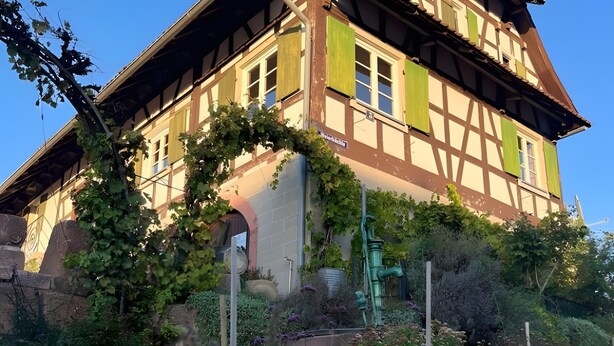 A traditional half-timbered building with a steep roof, green shutters, and a stone base. - Apartment 'Klein' with Shared Garden and Wi-Fi (Offenburg)