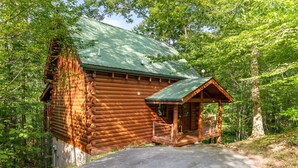 A wooden cabin with a green roof, surrounded by trees. - Mountain Oasis (Sevierville)