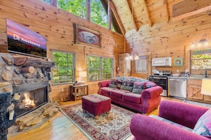 A cozy log cabin interior with a stone fireplace, a red sofa, and a kitchen area.