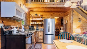 A wooden cabin kitchen with a stove, microwave, refrigerator, and dining table. - Mountain Oasis (Sevierville)