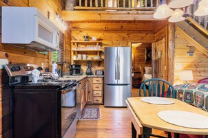 A wooden cabin kitchen with a stove, microwave, refrigerator, and dining table.