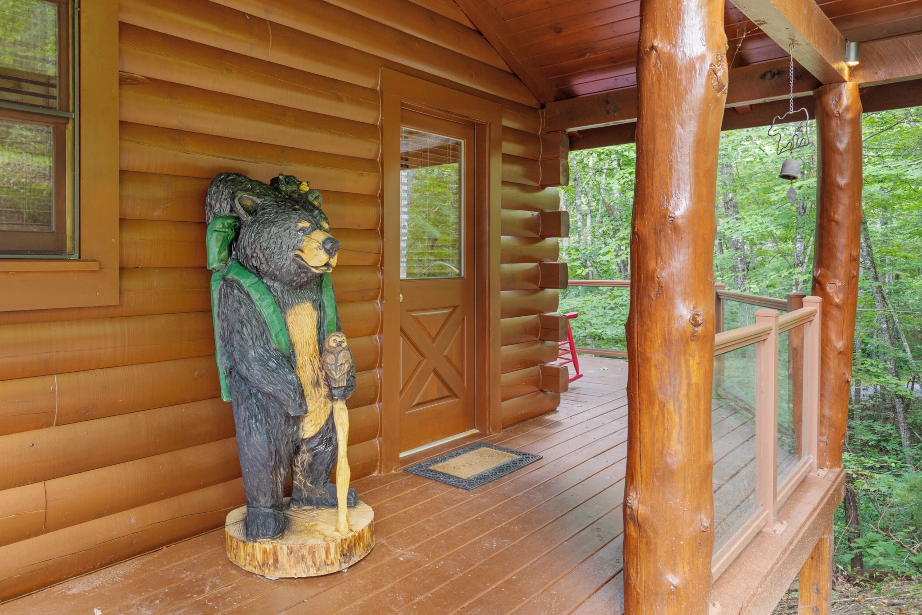 Una cabaña de madera con un porche, una estatua de oso y una puerta con ventana.