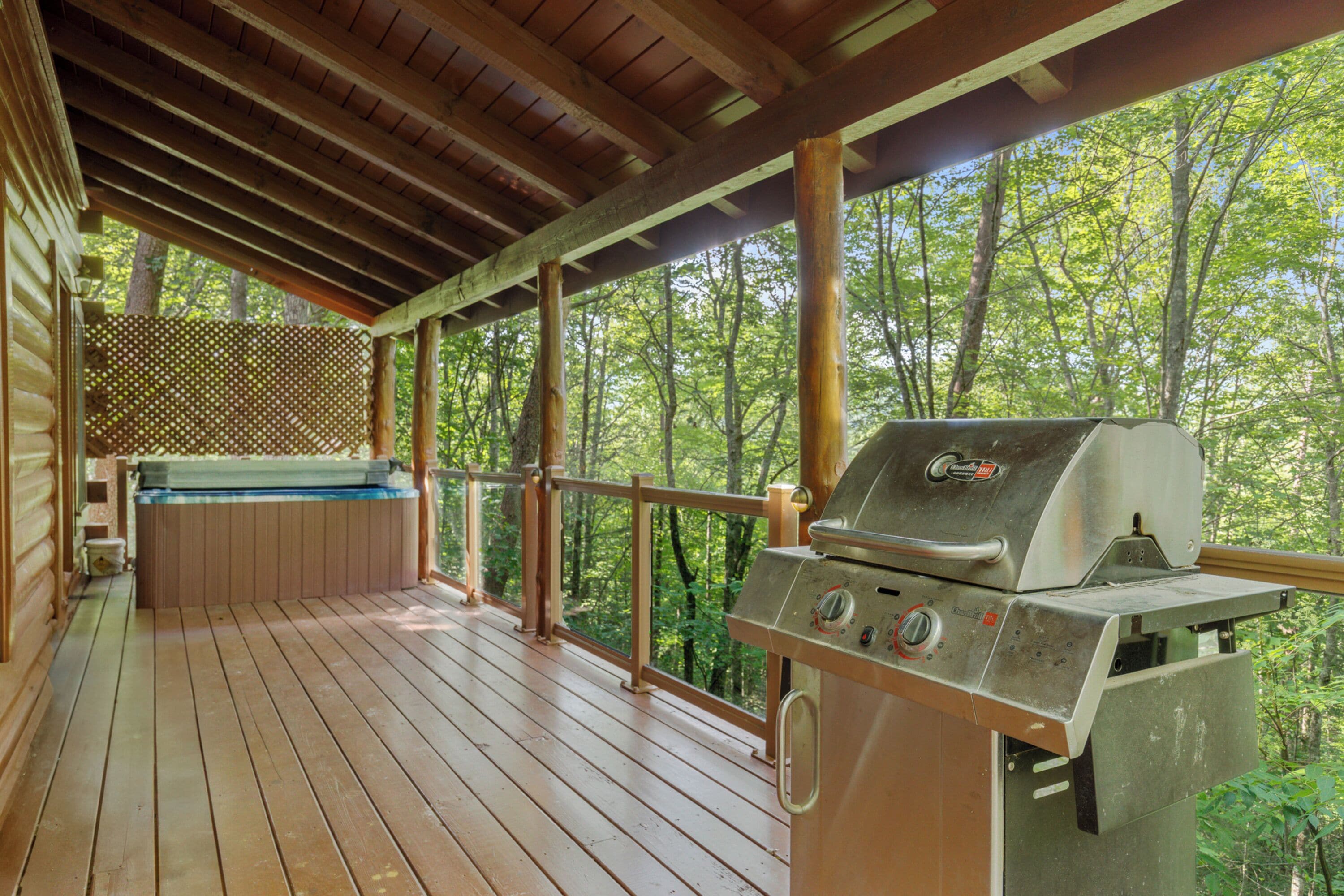 Een houten terras met een jacuzzi en een barbecue.