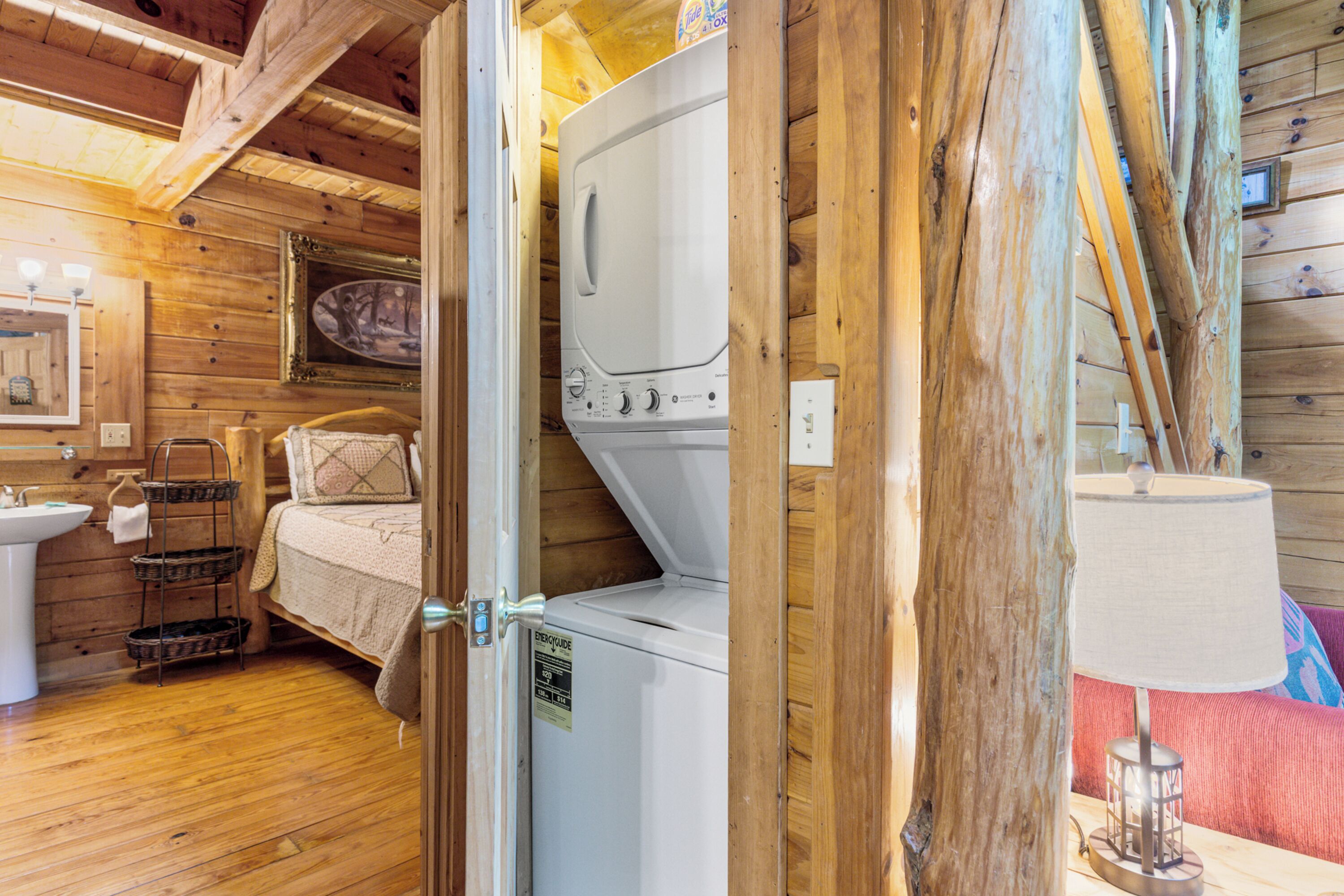 L’intérieur d’une cabane en bois, avec un lave-linge, un évier, un lit et une lampe.