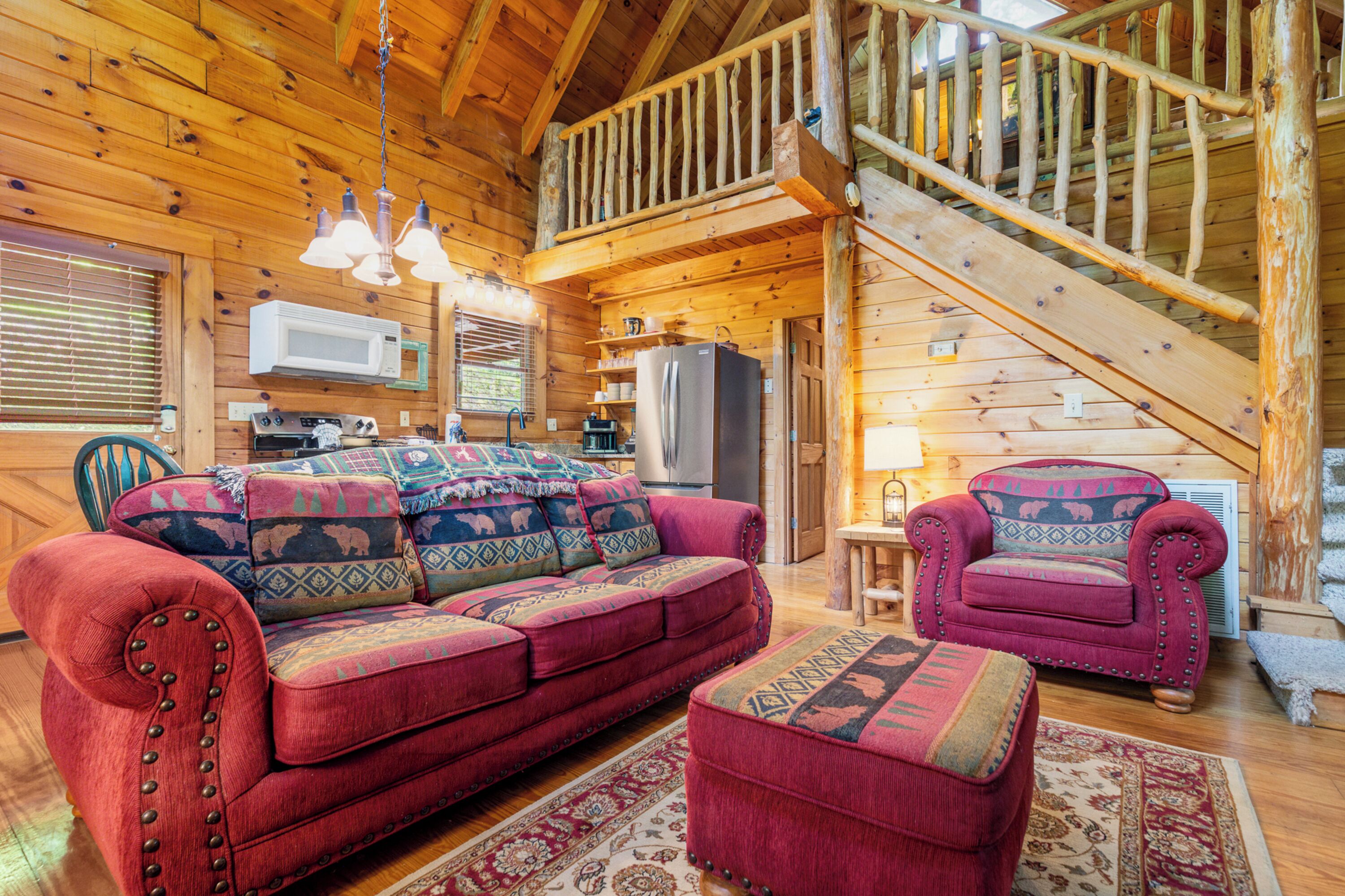 A cozy cabin interior with a wooden interior, a sofa, a chair, a kitchen area, and a staircase.