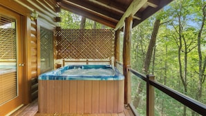 A wooden deck with a hot tub, wooden railings, and a view of a forest. - Mountain Oasis (Sevierville)