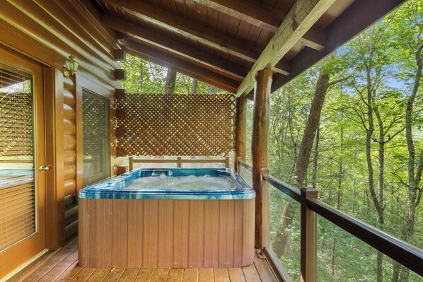 A wooden deck with a hot tub, wooden railings, and a view of a forest. - Mountain Oasis (Sevierville)
