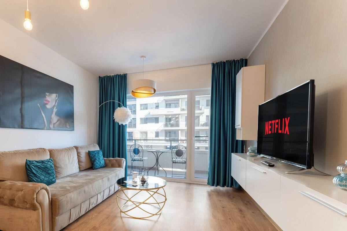 A modern living room with a sofa, a coffee table, a TV, and a large window with curtains.
