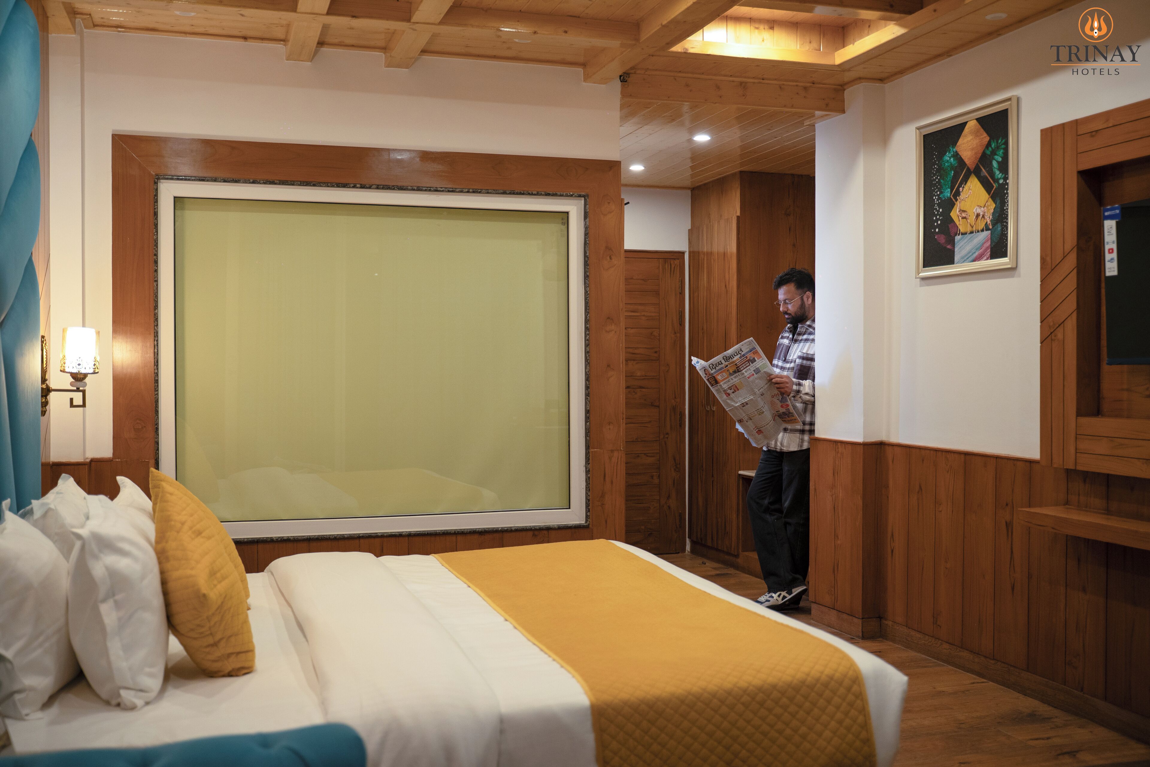 Une chambre d’hôtel avec un grand lit, des boiseries, une grande fenêtre et un tableau au mur.