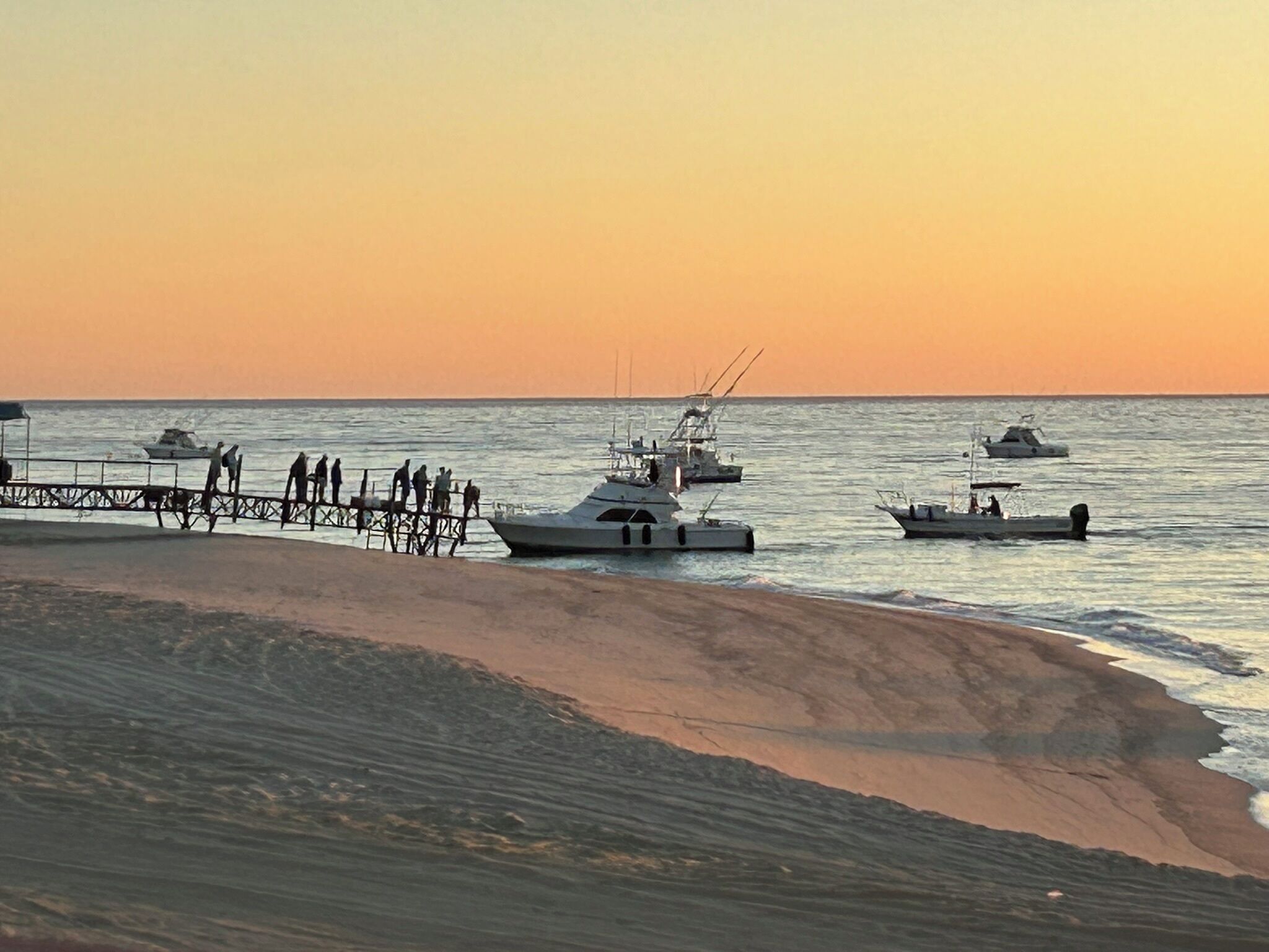 A pier with boats and people at sunset.