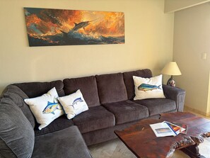 Ein Wohnzimmer mit einem dunkelbraunen Sofa, zwei Zierkissen, einem Holztisch und einem Bild von einem Fisch an der Wand.