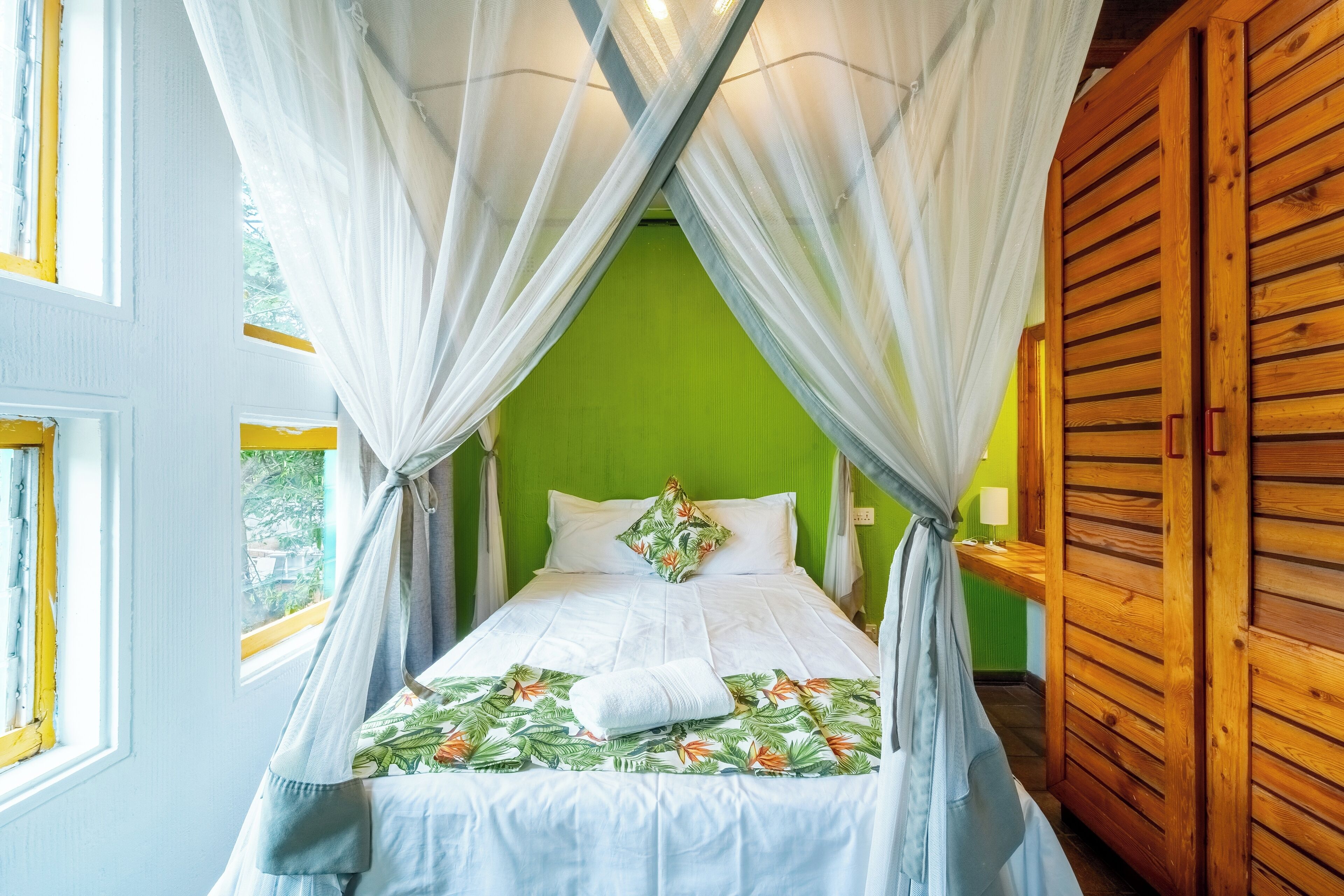 Una cama individual con dosel, pared verde y muebles de madera.