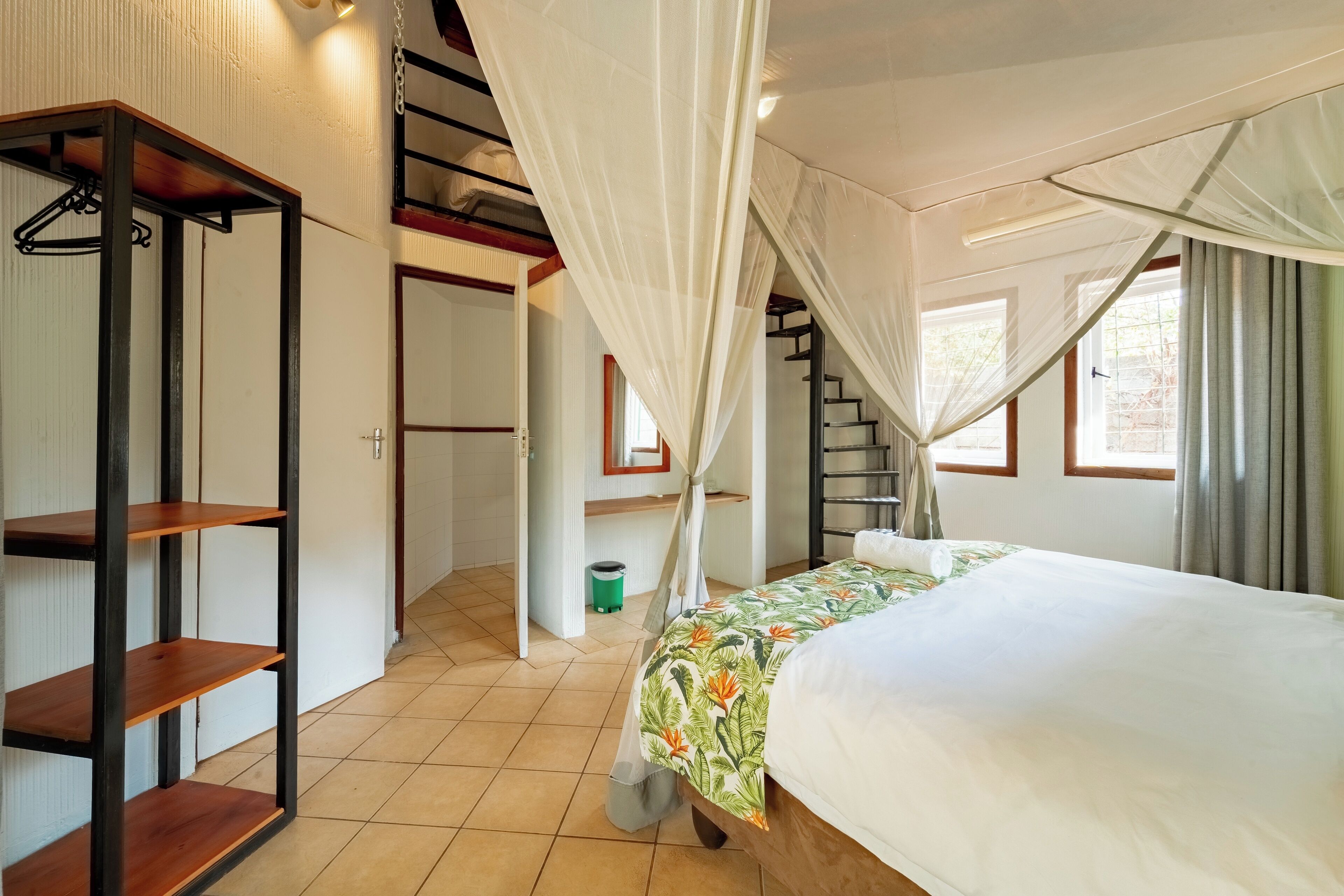 A bedroom with a bed, a wooden shelf unit, a staircase, and a window with curtains.