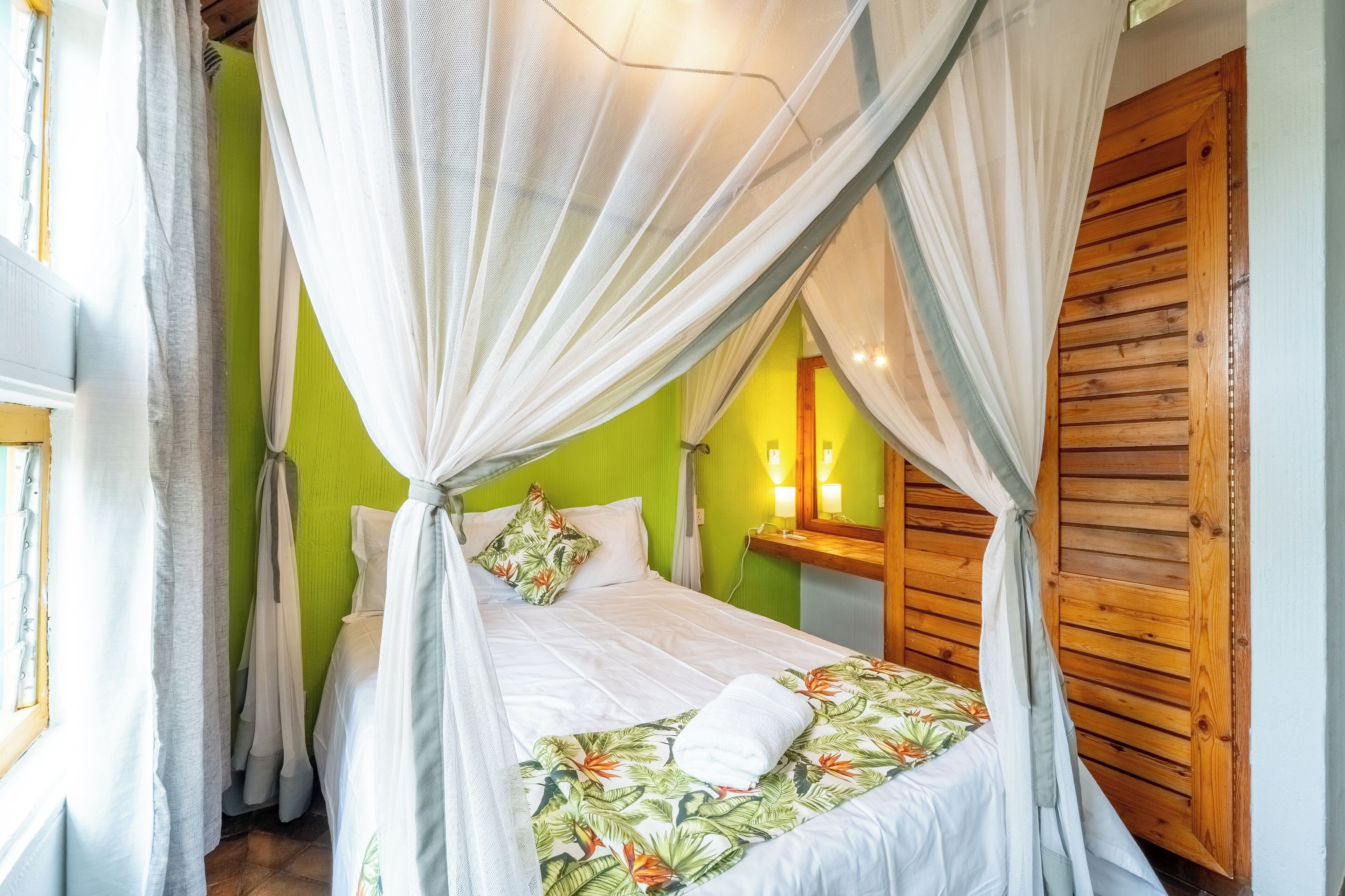 Quarto com cama sob dossel, paredes verdes e painéis de madeira.
