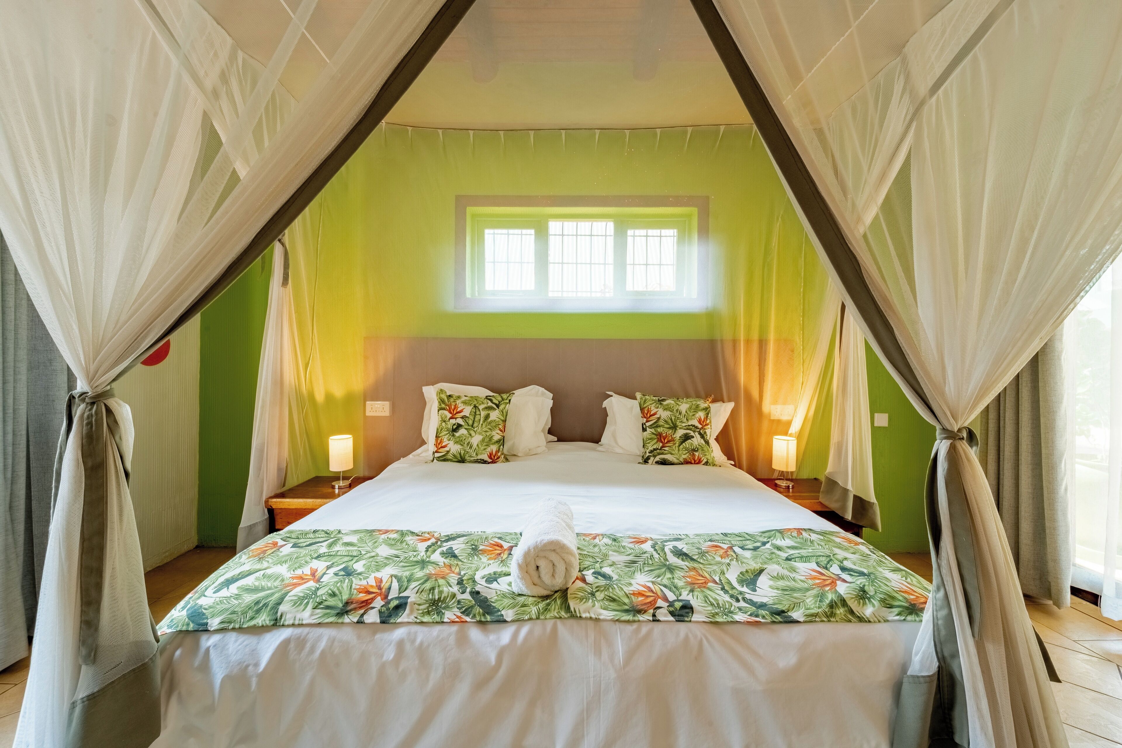 A bed with a floral bedspread, a rolled towel, and a window with bars.