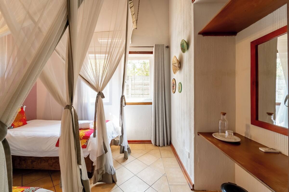 A room with a bed, a bedside table, a mirror, and a window with curtains.