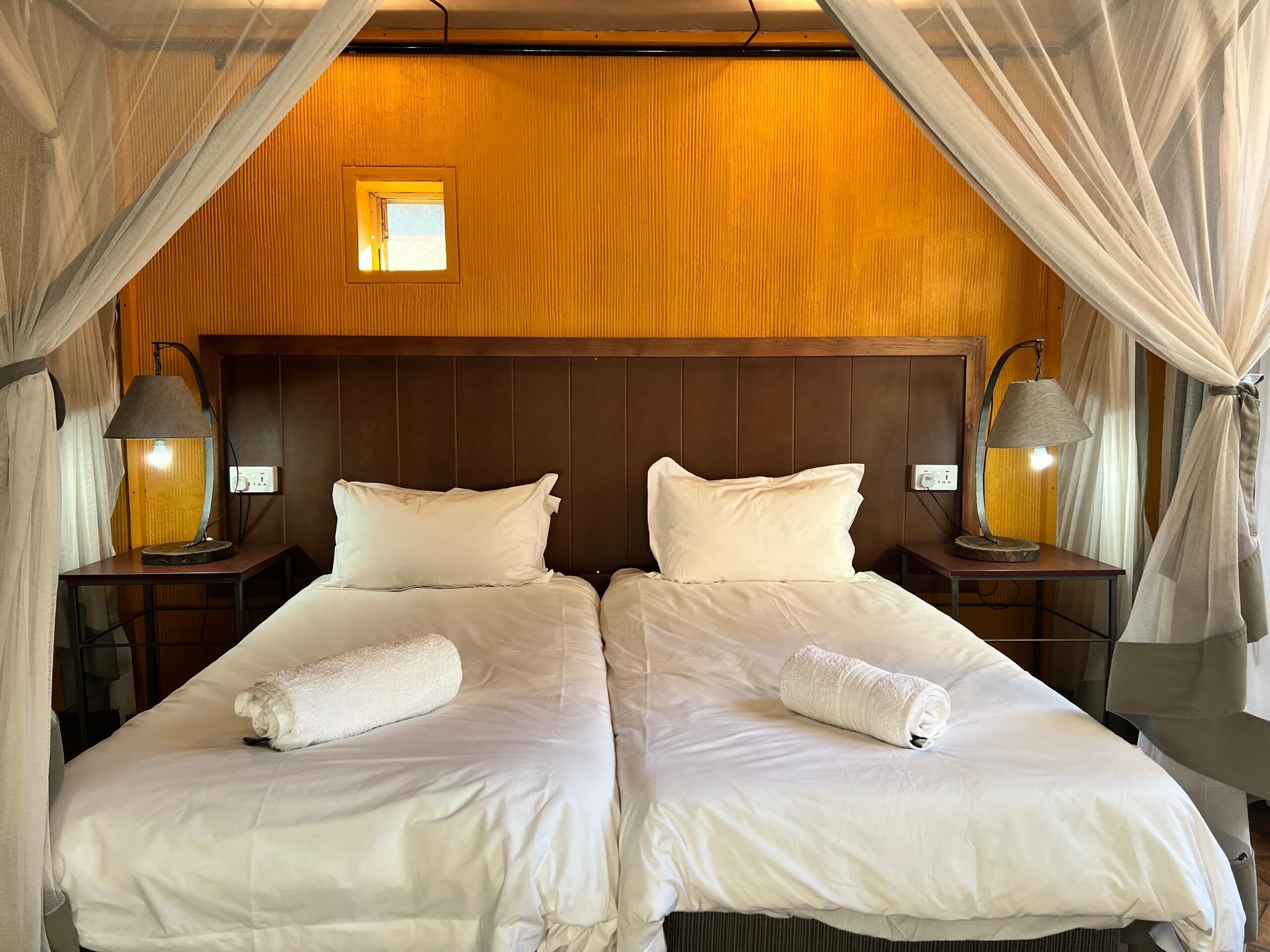 A double bed with white linens, two bedside lamps, a small window, and a wooden headboard.