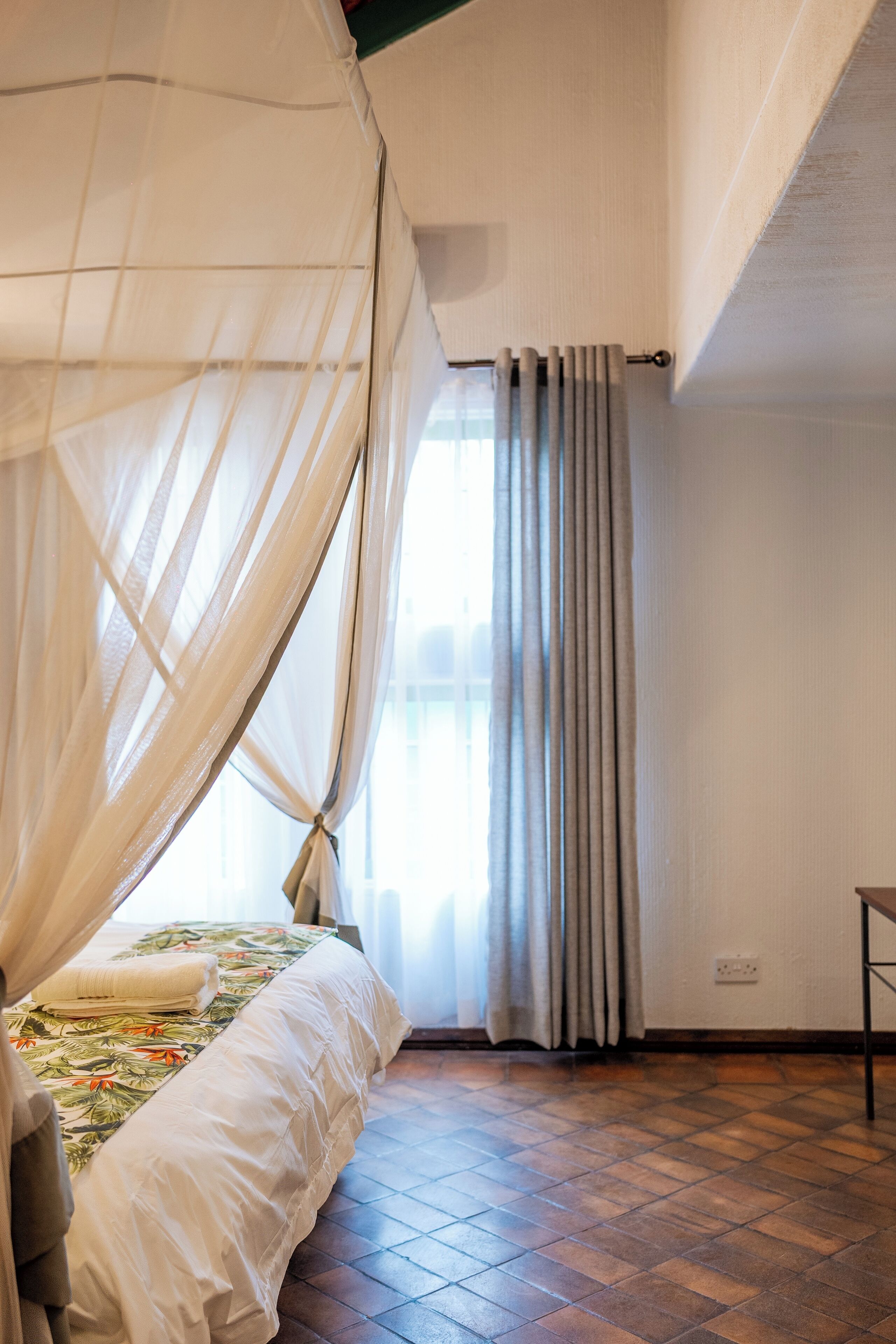 Un dormitorio con cama, mosquitera y ventana con cortinas.