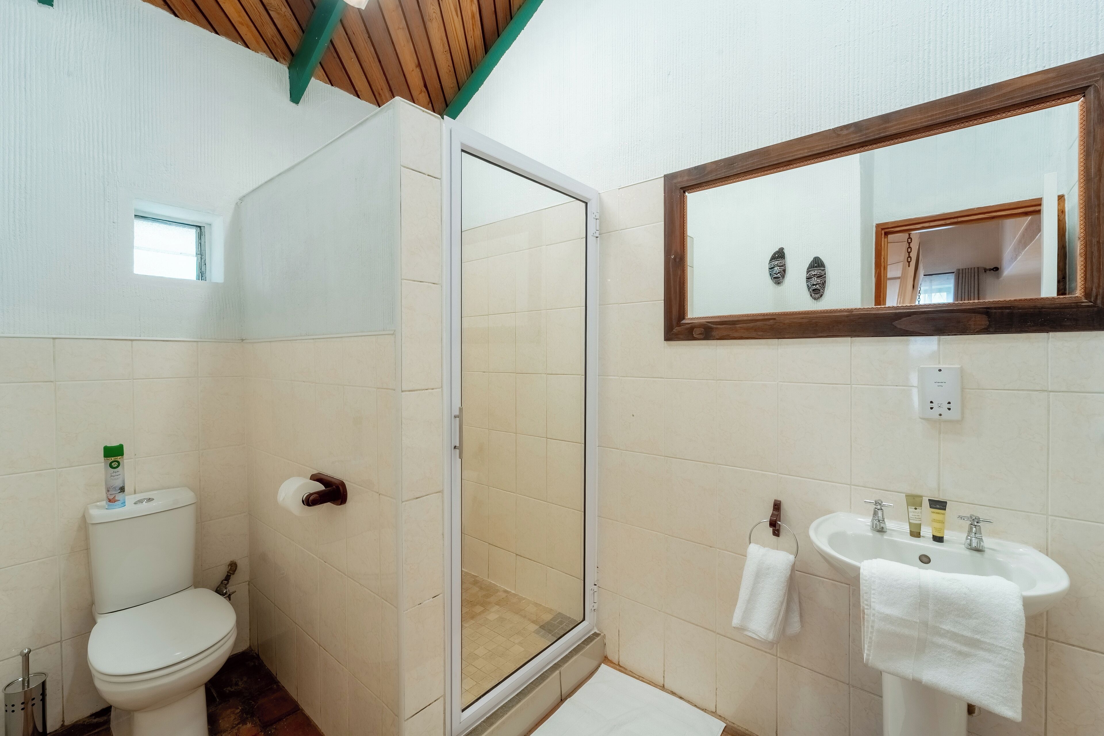 A bathroom with a toilet, shower, sink, and a mirror.