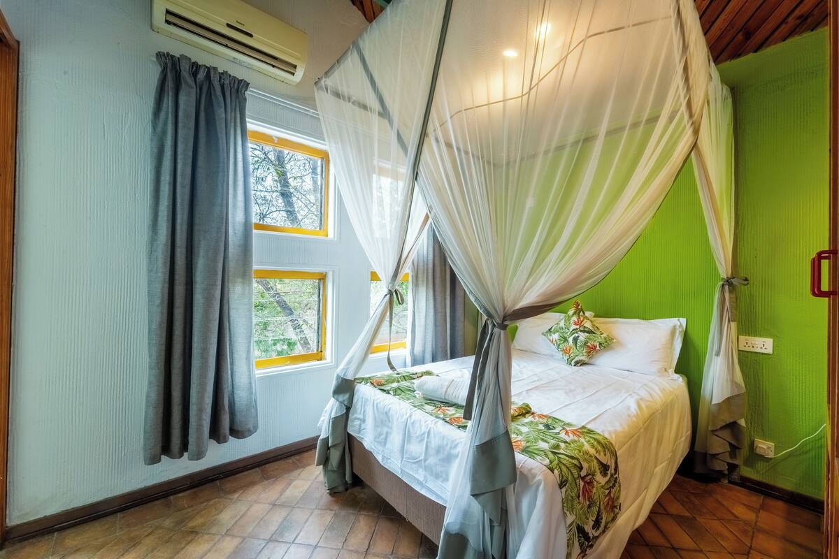 A room with a bed, a window with curtains, an air conditioning unit, and a green wall.