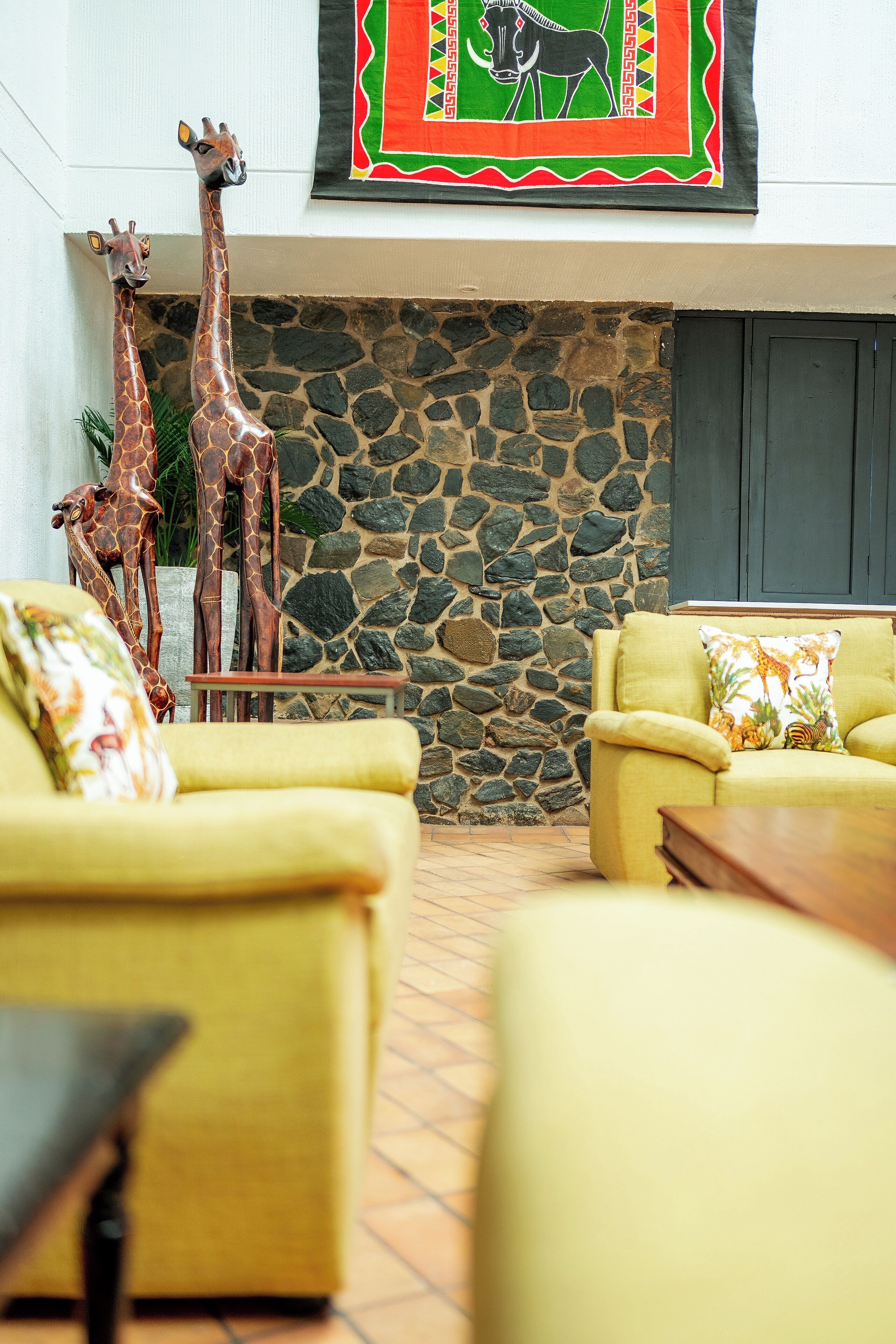 A room with a stone wall, two giraffe sculptures, and yellow sofas with patterned cushions.