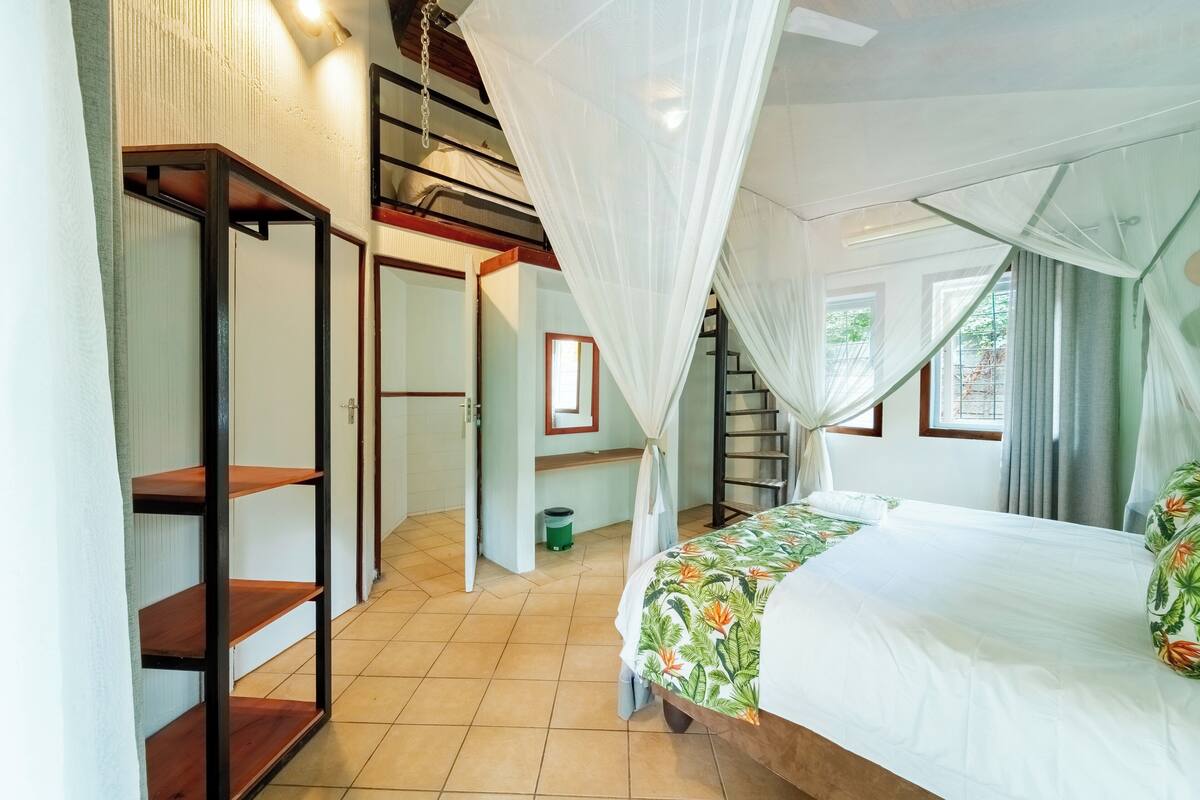 A bedroom with a bed, a wardrobe, a staircase, and a window.