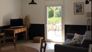 A living room with a TV on a wooden table, a sofa, and a door leading to a balcony. - House in Provence, 15 minutes from the beach, 20 minutes from Aix and Marseille. (Auriol)