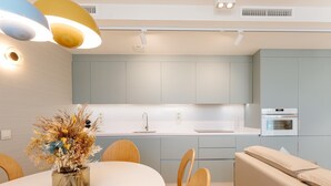 A modern kitchen with light blue cabinets, a white countertop, and a built-in oven. There is a dining table with chairs and a vase of dried flowers. - Apartment 3 bedroom | ground floor| mountain view (La Caleta)