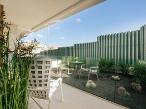 A modern outdoor patio with a glass wall, white chairs, and cacti.