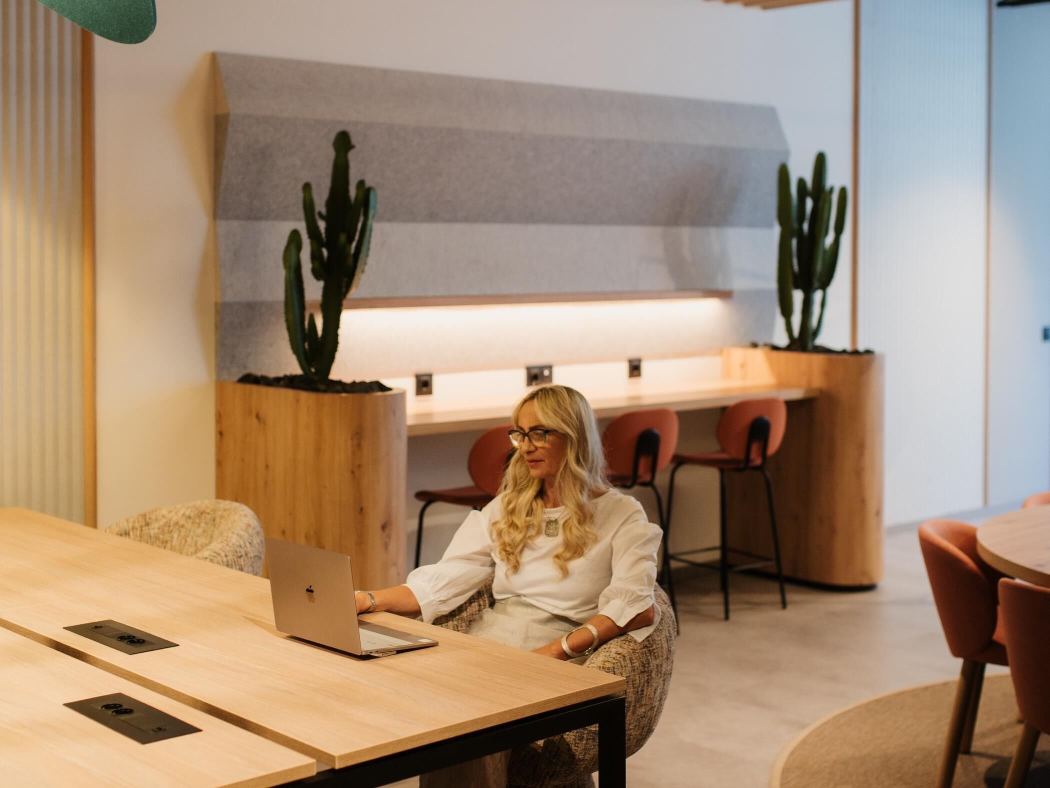 Un espace de bureau moderne avec une table en bois, un ordinateur portable et deux cactus en pot.