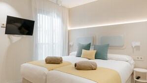 A hotel room with two beds, a flat-screen TV mounted on the wall, a bedside table, and a window with curtains. - Apartment 3 bedroom | ground floor| mountain view (La Caleta)