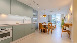 A modern kitchen with light green cabinets, a white countertop, and a built-in oven. There is a dining area with a wooden table and chairs, and a large window offering a view of the outdoors.