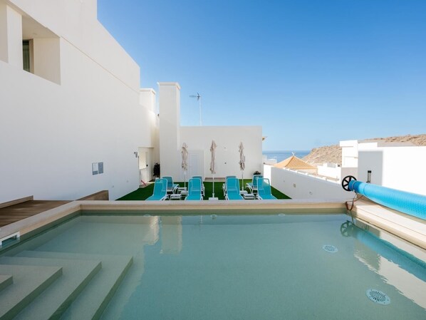 Zona de piscina en la azotea con sillones reclinables azules y una vista despejada del mar.