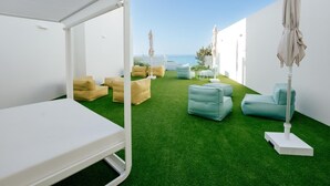 Une terrasse sur le toit avec un lit blanc, de l’herbe artificielle verte et plusieurs coins salon agrémentés de coussins.