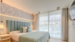 Camera d'albergo moderna con un letto grande, un comodino e vista su una piscina attraverso tende leggere.