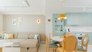 A modern living room with a beige sofa, a dining table with chairs, and a kitchen area with light blue cabinets and a white countertop. - Apartment 2 bedroom | ground floor| mountain view (La Caleta)