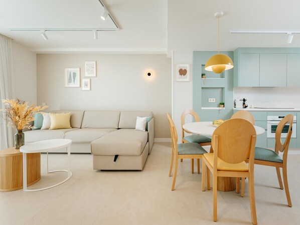Een moderne woonkamer met een hoekbank, een eettafel met stoelen, en een keuken met lichtblauwe kastjes.