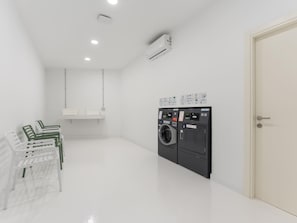Een schone, moderne wasruimte met een wasmachine en droger, een witte deur en een bank met groene en witte stoelen.