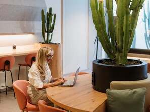 Une personne est assise à une table en bois et utilise un ordinateur portable. On aperçoit, en arrière-plan, un grand cactus en pot.