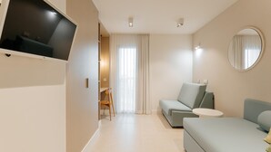 Ein modernes Hotelzimmer mit Flachbildfernseher, einer Couch, einem Sessel, einem kleinen Tisch und einem runden Spiegel.