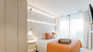 Ein modernes Hotelzimmer mit einem großen Bett, einem Schrank, einem Nachttisch und einem großen Fenster mit Vorhängen.