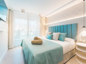 A modern hotel room with a large bed, a bedside table, and a view through sheer curtains.