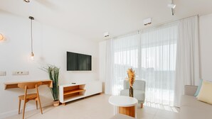 Un salon moderne avec un canapé blanc, une table basse ronde, un téléviseur fixé au mur et un bureau avec une chaise.