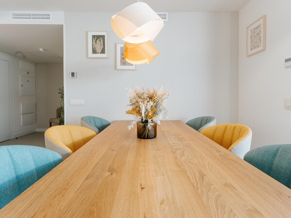 A modern dining area with a wooden table, yellow and teal chairs, and a vase of dried flowers. - Exclusive penthouse huge terrace in La Caleta (La Caleta)