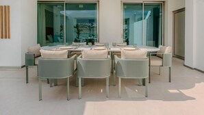 A modern dining area with a round table and six chairs, large glass doors leading to a balcony, and a minimalist interior design.